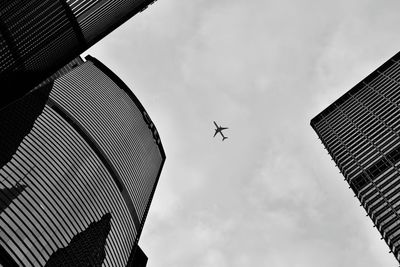 Low angle view of airplane flying over buildings against sky