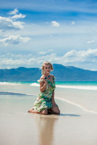 Woman sitting at beach against sky