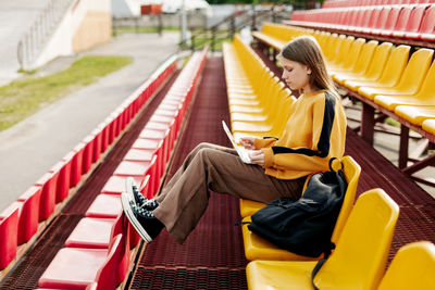 A young girl is doing her homework using a laptop in the stands of the stadium.