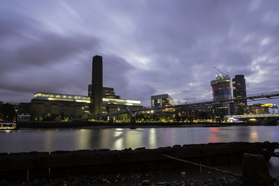 Illuminated city by river against sky at night