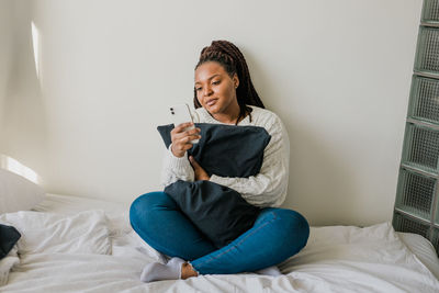 Young woman using mobile phone while lying on bed at home