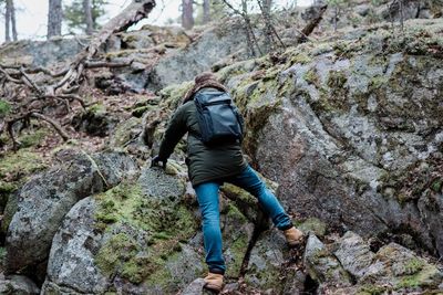Man climbing a rock whilst hiking in a forest in winter