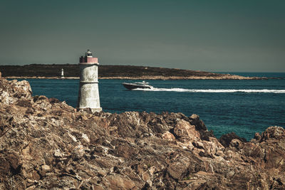 Lighthouse on  rocks in the north of sardinia with a boat crossing