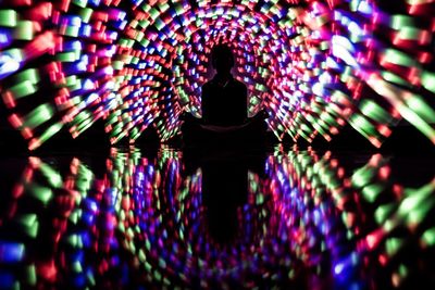 Rear view of silhouette woman sitting on illuminated multi colored lights