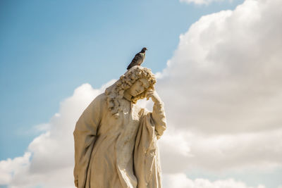Low angle view of statue against sky with pidgeon on head