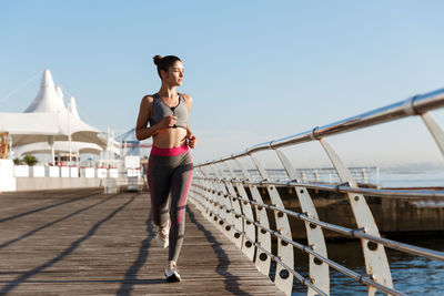 Woman running by railing against sky