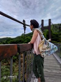 Side view of woman standing by railing against sky