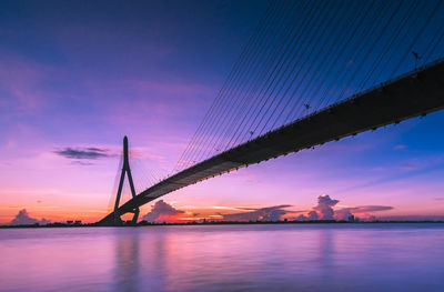 Silhouette bridge over sea against dramatic sky during sunset