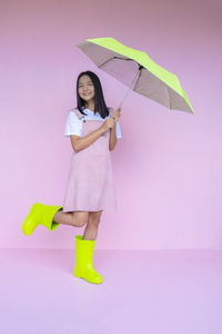 Full length portrait of a smiling young woman standing against gray background