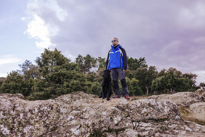 Man with dog standing on rock against sky