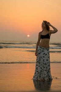 Full length of woman standing at beach against sky during sunset