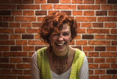 Portrait of cheerful young woman against brick wall