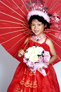Portrait of cute flower girl wearing red dress while holding bouquet and traditional umbrella