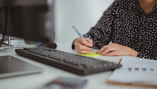 Midsection of woman writing on adhesive note at desk