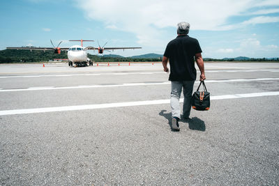 Rear view of man on airport runway against sky