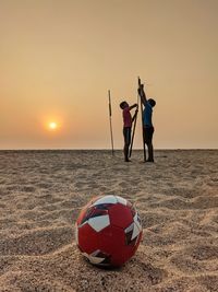 People on soccer field at beach against sky during sunset