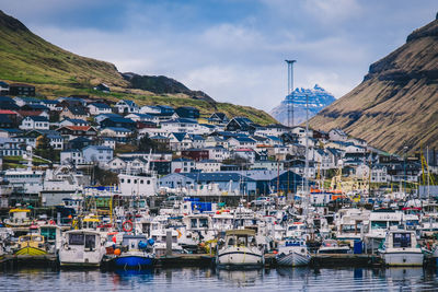 Sailboats moored at sea by townscape against sky