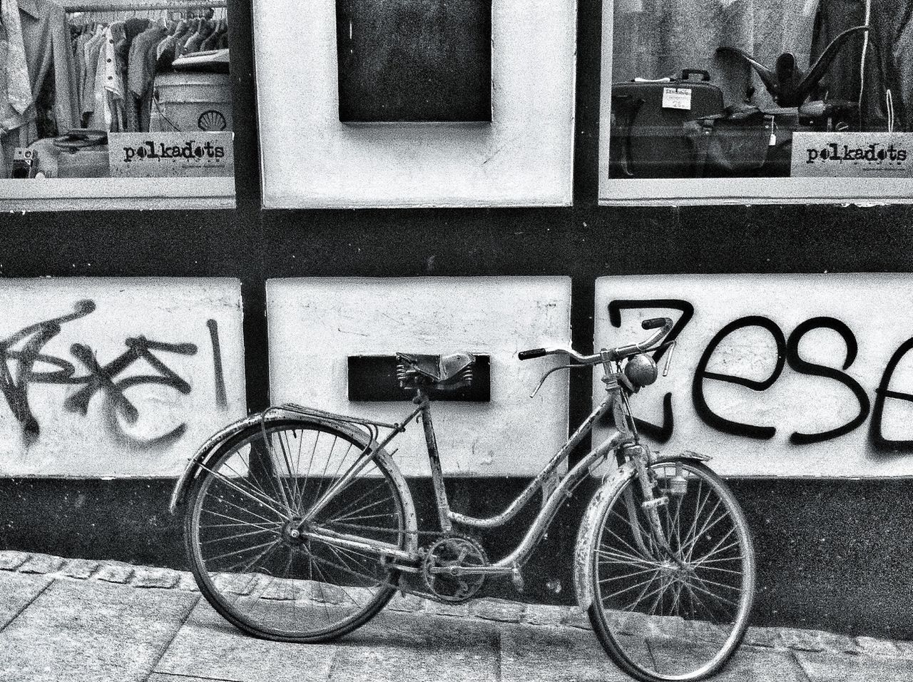 bicycle, transportation, land vehicle, mode of transport, stationary, parked, parking, building exterior, architecture, built structure, wall - building feature, sidewalk, street, graffiti, day, outdoors, no people, wheel, wall, leaning