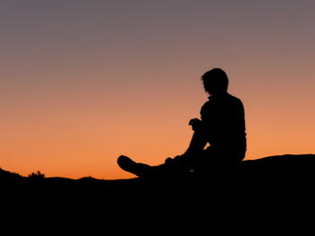 Silhouette of man sitting against orange sky