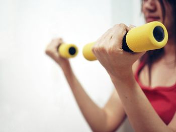 Midsection of woman lifting dumbbells in gym