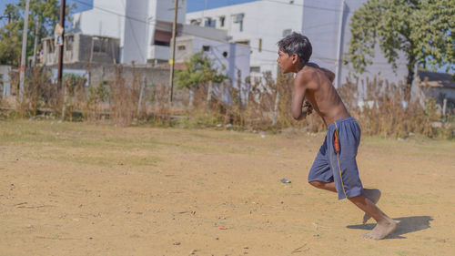 Full length side view of shirtless boy playing on field during sunny day