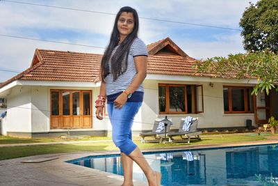 Portrait of young woman standing by swimming pool against building