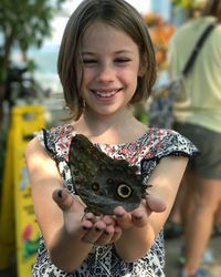 Happy girl holding butterfly while standing on footpath