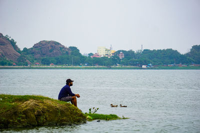 Man sitting by lake against clear sky