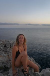 Portrait of smiling woman sitting on beach against sky