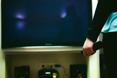 Midsection of woman holding remote control while standing at home