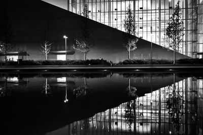 Illuminated building by lake against sky at night