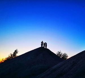 Silhouette men standing on mountain against clear blue sky