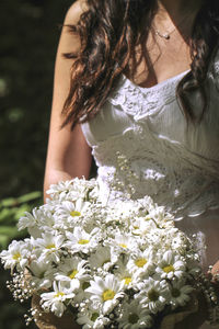 Midsection of woman against white flowering plants