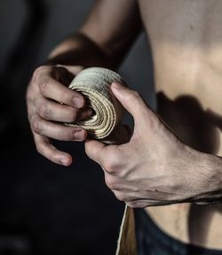 Midsection of shirtless man rolling bandage at home