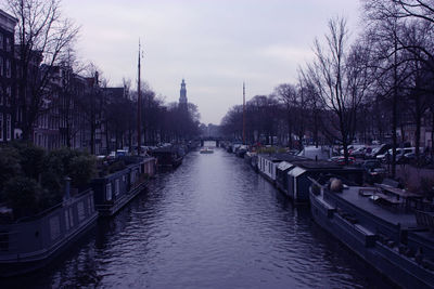Canal amidst bare trees in city against sky