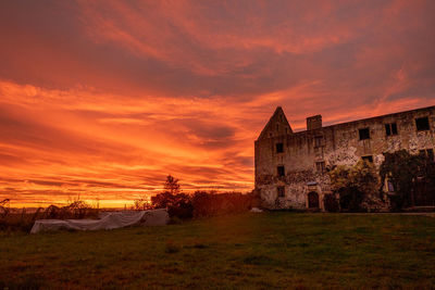 Old building on field against orange sky