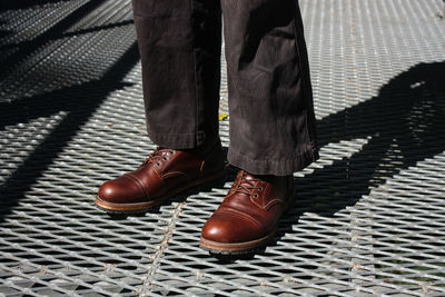 Low section of man standing on metal grate during sunny day