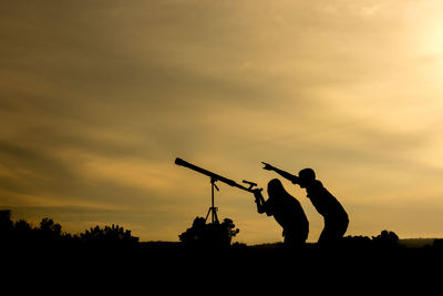 Silhouette people looking through binoculars against sky during sunset