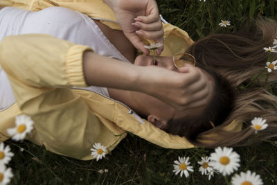 High angle view of woman lying amidst daisies on field