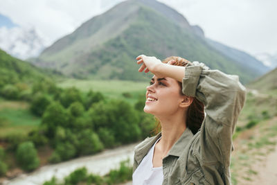 Young woman drinking coffee while standing against mountain