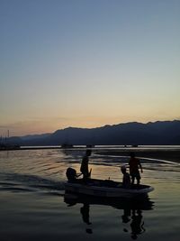 Silhouette men on shore against sky during sunset