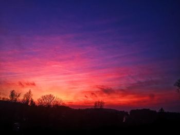 Silhouette trees against dramatic sky during sunset