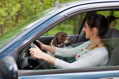 Side view of woman driving with dog in car