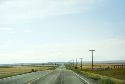 Empty road amidst field against sky