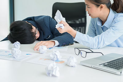 Tensed business colleagues with crumpled paper at desk in office