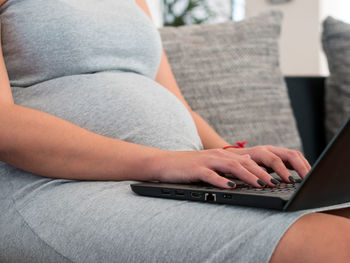 Midsection of woman using laptop while sitting on sofa at home