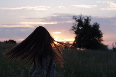 Side view of woman with tousled hair standing on field at sunset