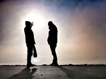 Silhouette men standing on beach against sky during sunset