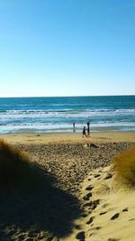 People walking on beach against clear blue sky