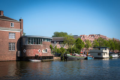 Buildings by river against clear blue sky